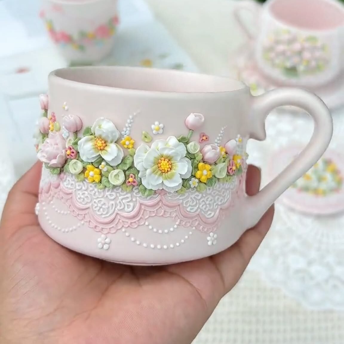 Pink floral ceramic mug with its curved handle and raised pastel flower-and-lace decoration