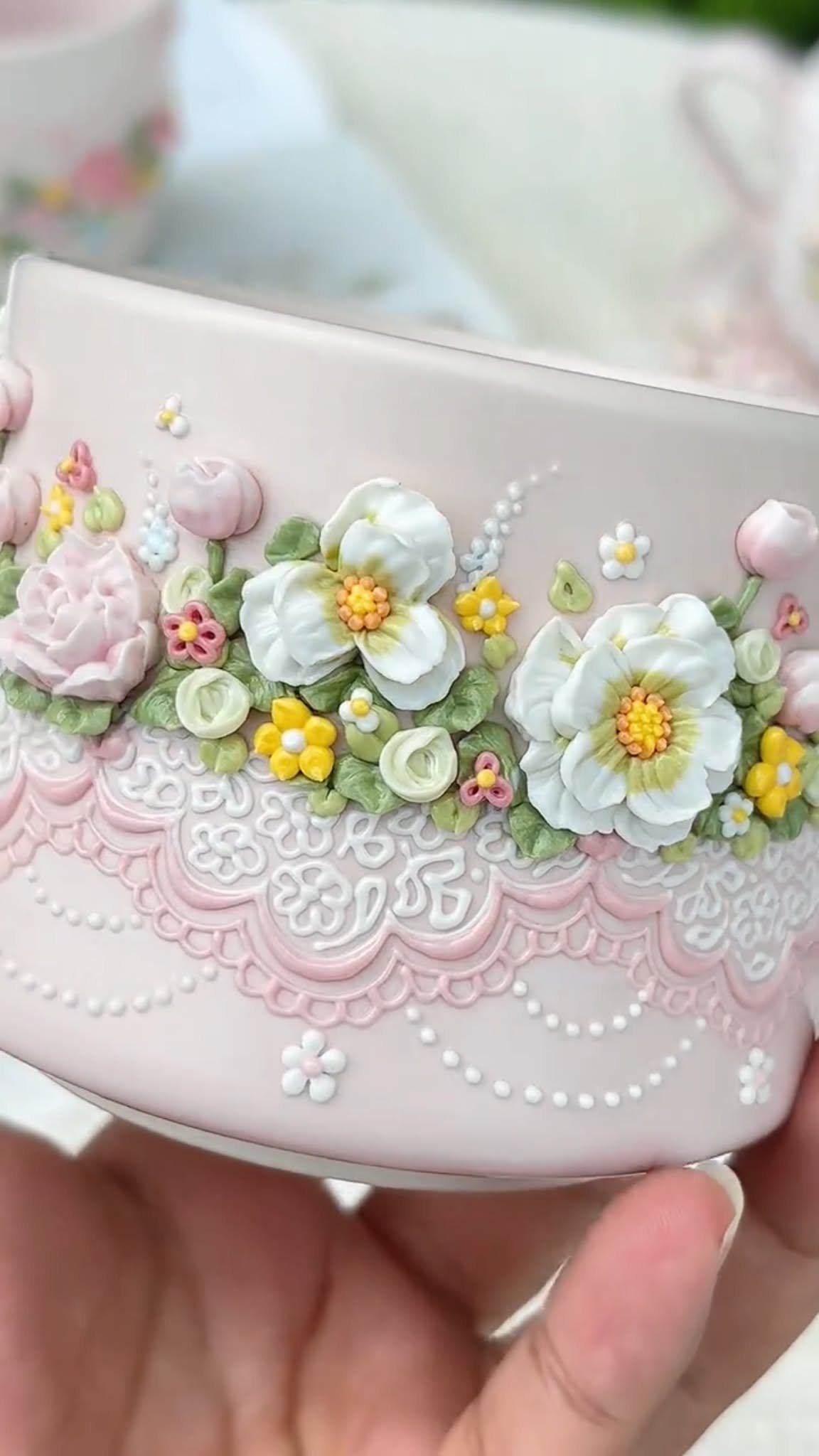 Close-up of raised white blossoms, pink buds and lace-like relief on a pink ceramic mug